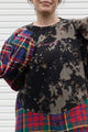 person wearing bleached sweater that is sewn together with red plaid shirt, upcycled in canada detail shot of 'no labels, just vibes.' embroidery