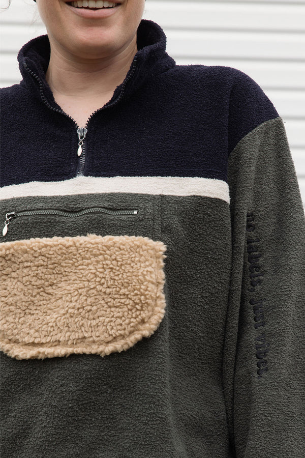 person wearing a fleecy half zip pull over, green and black, upcycled in canada, detail shot of 'no label, just vibes.' embroidery