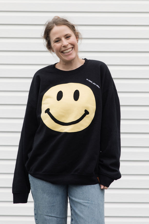 Person wearing a black sweatshirt with a yellow smiley face design, upcycled in canada