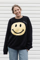 Person wearing a black sweatshirt with a yellow smiley face design, upcycled in canada
