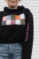 Person wearing a black hoodie with a colorful square design, upcycled in canada, featuring 'no labels, just vibes.' embroidery on the sleeve