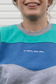 Person wearing a teal, blue and grey vintage sweater, upcycled in canada detail shot of 'no labels, just vibes.' embroidery