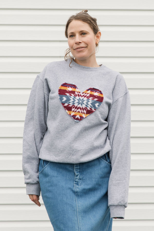 woman wearing geometric printed heart, stitched onto light grey sweater