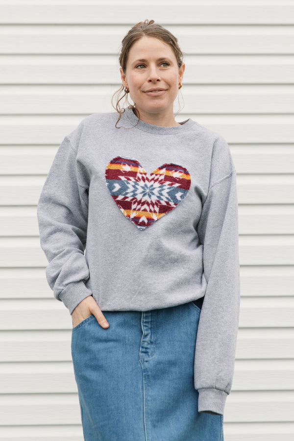 Person wearing a gray sweatshirt with a colorful heart design against a white background