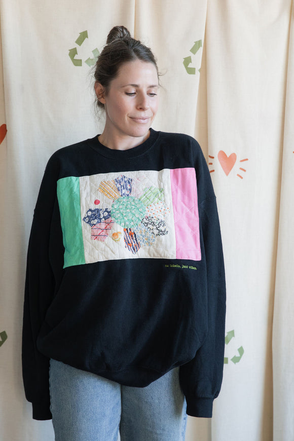 Person wearing a black sweatshirt with colorful patchwork design, upcycled in canada