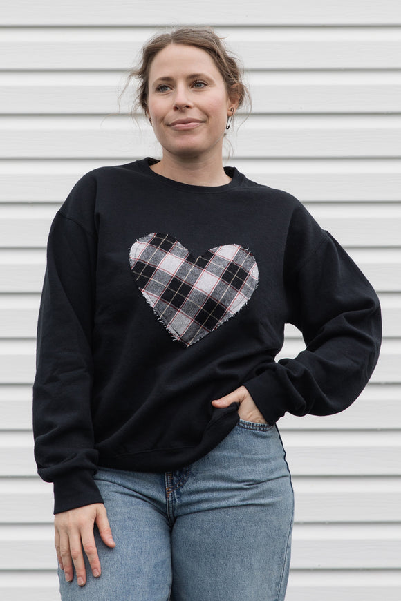 Person wearing a black sweatshirt with a black, white & red plaid heart design