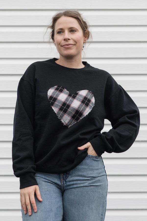 Person wearing a black sweatshirt with a black, white & red plaid heart design