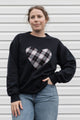 Person wearing a black sweatshirt with a black, white & red plaid heart design