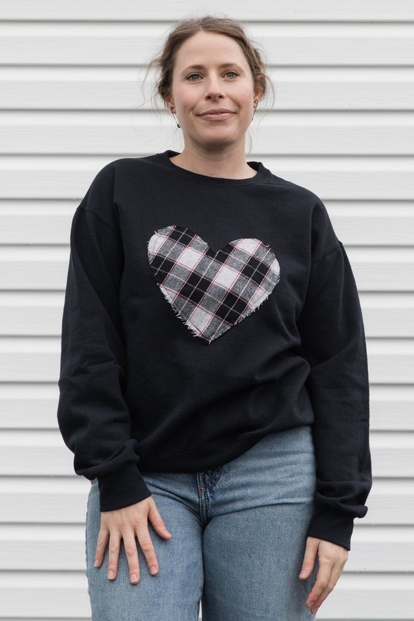Person wearing a black sweatshirt with a black, white & red plaid heart design