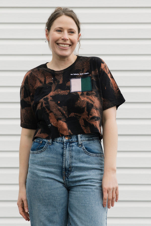 Woman wearing a tie-dye shirt and jeans standing in front of a white wall.