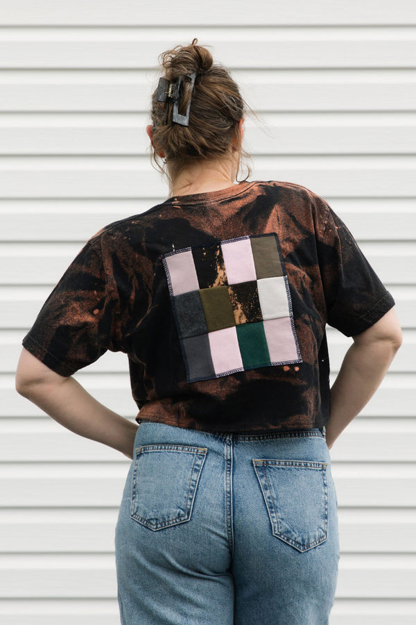 Person wearing a black t-shirt with a colorful geometric pattern on the back, standing against a white wall.