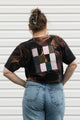 Person wearing a black t-shirt with a colorful geometric pattern on the back, standing against a white wall.
