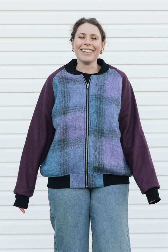 Person wearing a purple and blue plaid zip up jacket with plum sleeves, upcycled in canada