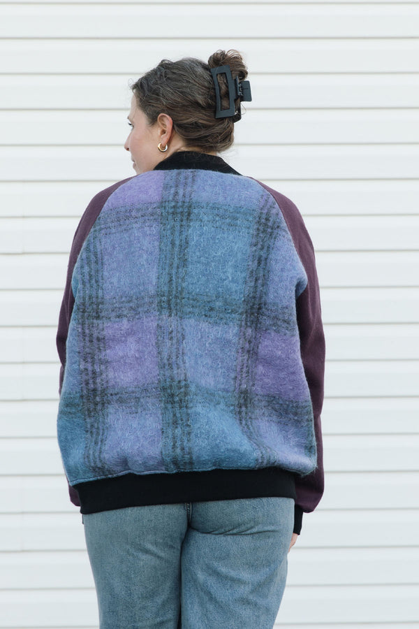 Person wearing a purple and blue plaid zip up jacket with plum sleeves, upcycled in canada