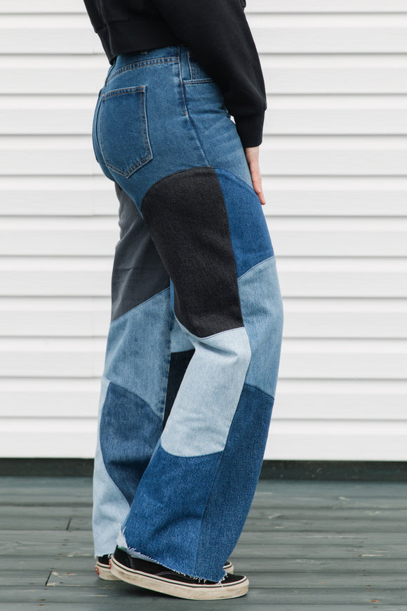 Person wearing patchwork jeans in front of a white wall.