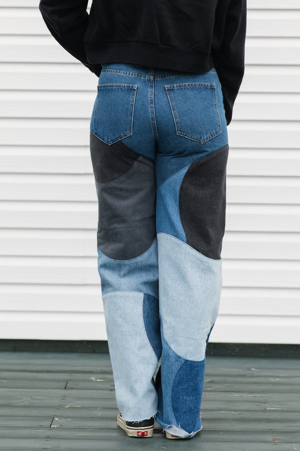 Person wearing patchwork jeans with blue and black patches against a white wall.