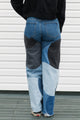Person wearing patchwork jeans with blue and black patches against a white wall.