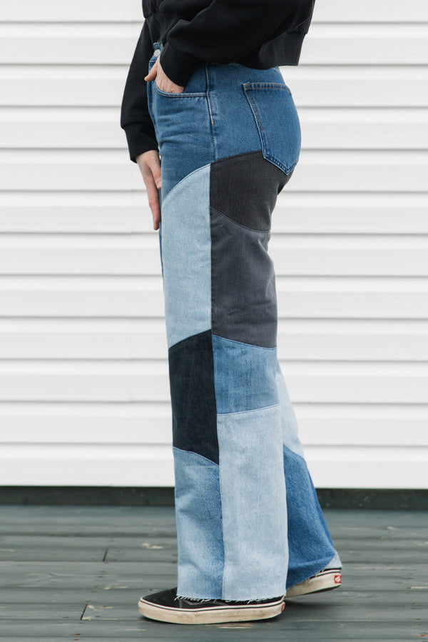 Person wearing patchwork jeans standing against a white wall.