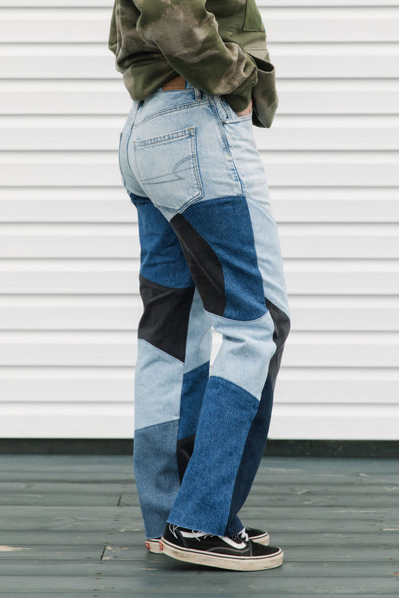 Person wearing patchwork jeans with a white wall background