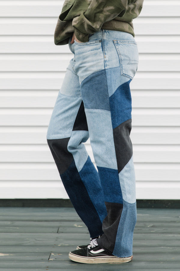 Person wearing patchwork jeans with a white wall background