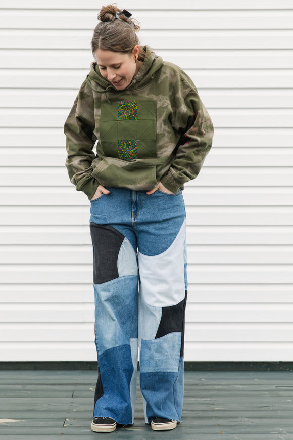 Person wearing a green hoodie with a patch and blue patchwork jeans against a white background