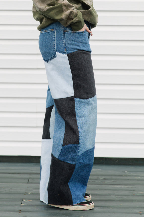 Person wearing patchwork jeans with a white wall background