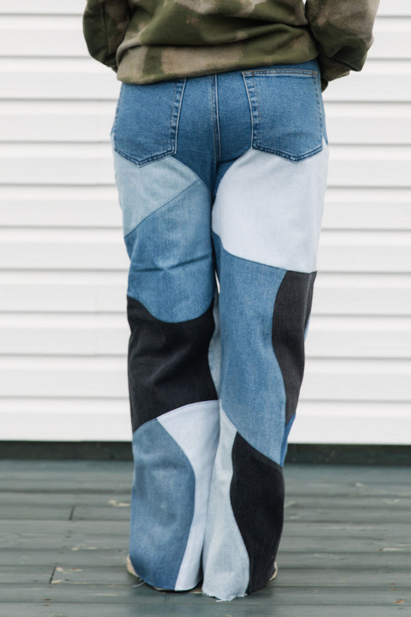 Person wearing patchwork jeans with blue, white, and black patches against a white wall.