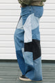 Person wearing patchwork jeans standing against a white wall.