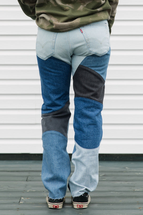 Person wearing blue jeans with black patches against a white wall.