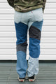 Person wearing blue jeans with black patches against a white wall.