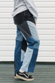 Person wearing a pair of patchwork jeans with black, blue, and gray colors against a white wall.