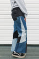 Person wearing a gray hoodie with colorful text and patchwork jeans standing against a white wall, upcycled in canada