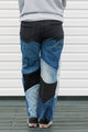 Person wearing a gray hoodie with colorful text and patchwork jeans standing against a white wall, upcycled in canada