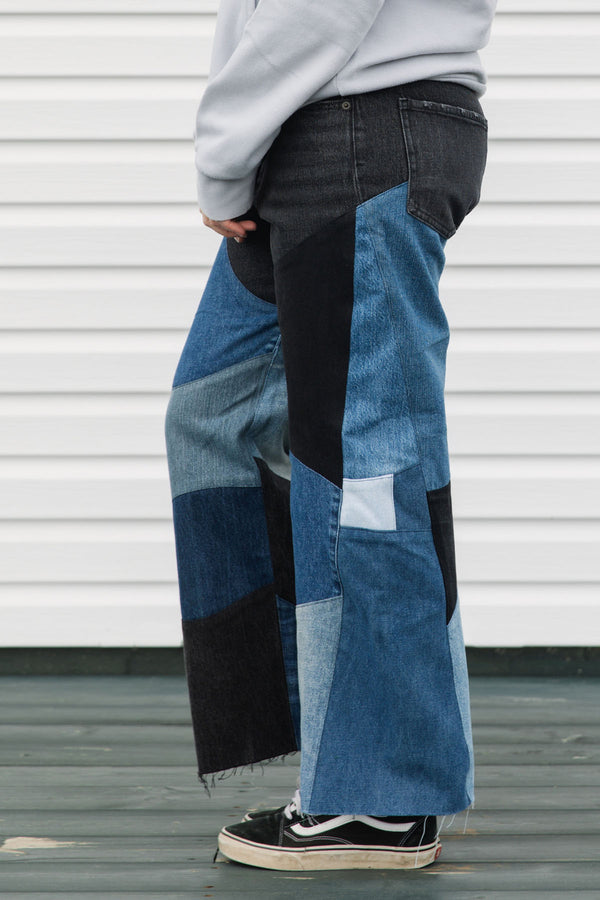 Person wearing a gray hoodie with colorful text and patchwork jeans standing against a white wall, upcycled in canada