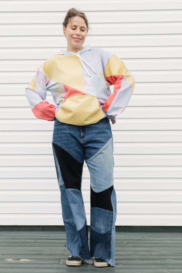 Person wearing a colorful sweater and patchwork jeans against a white background, upcycled in canada