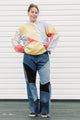 Person wearing a colorful sweater and patchwork jeans against a white background, upcycled in canada