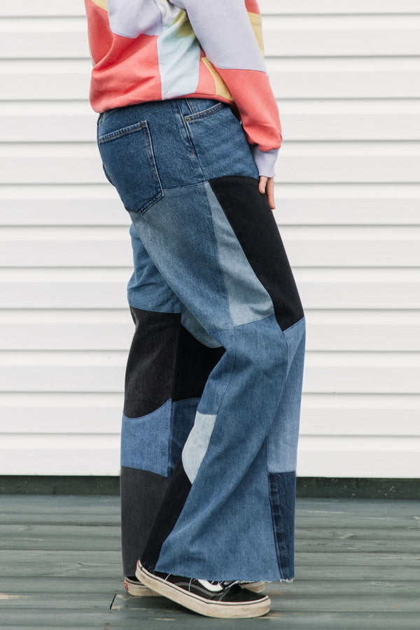 Person wearing a colorful sweater and patchwork jeans against a white background, upcycled in canada