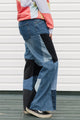 Person wearing a colorful sweater and patchwork jeans against a white background, upcycled in canada
