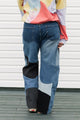Person wearing a colorful sweater and patchwork jeans against a white background, upcycled in canada