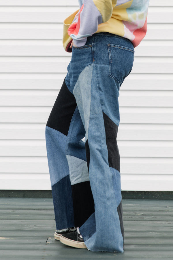 Person wearing a colorful sweater and patchwork jeans against a white background, upcycled in canada