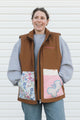 Woman wearing a brown quilted vest with floral and cartoon designs on a white background