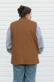 Person wearing a brown vest over a gray shirt with a white background