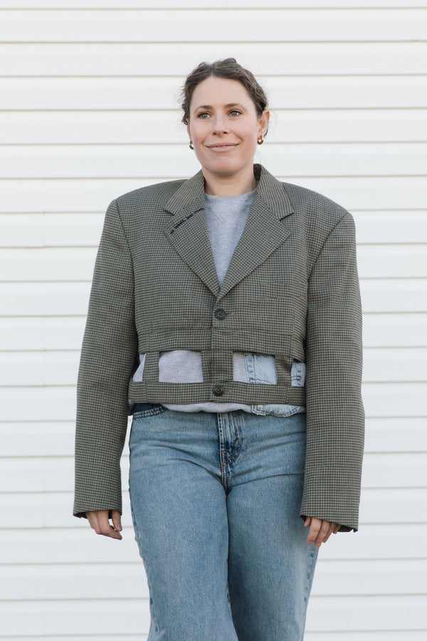 Person wearing a green checkered jacket over a gray shirt with blue jeans against a white background