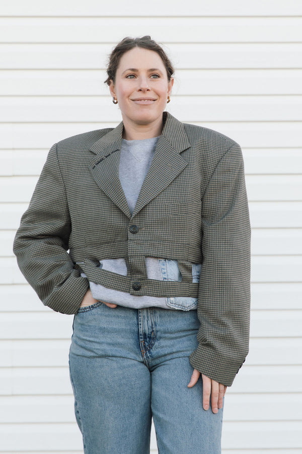 Person wearing a green blazer over a gray shirt and blue jeans against a white background