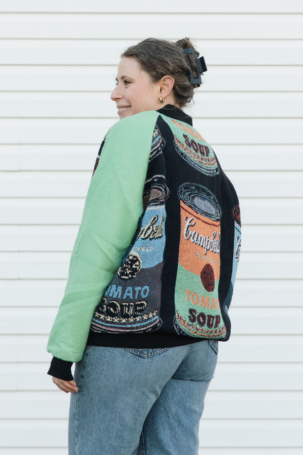 Person wearing a colorful vintage-style jacket with soup can designs against a white background