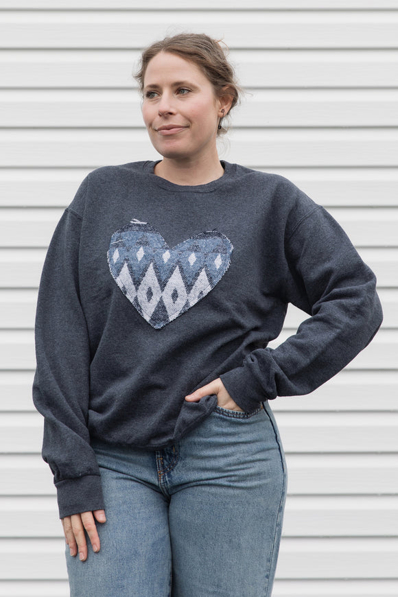 Woman wearing a charcoal grey sweatshirt with a blue heart design, sewn in canada