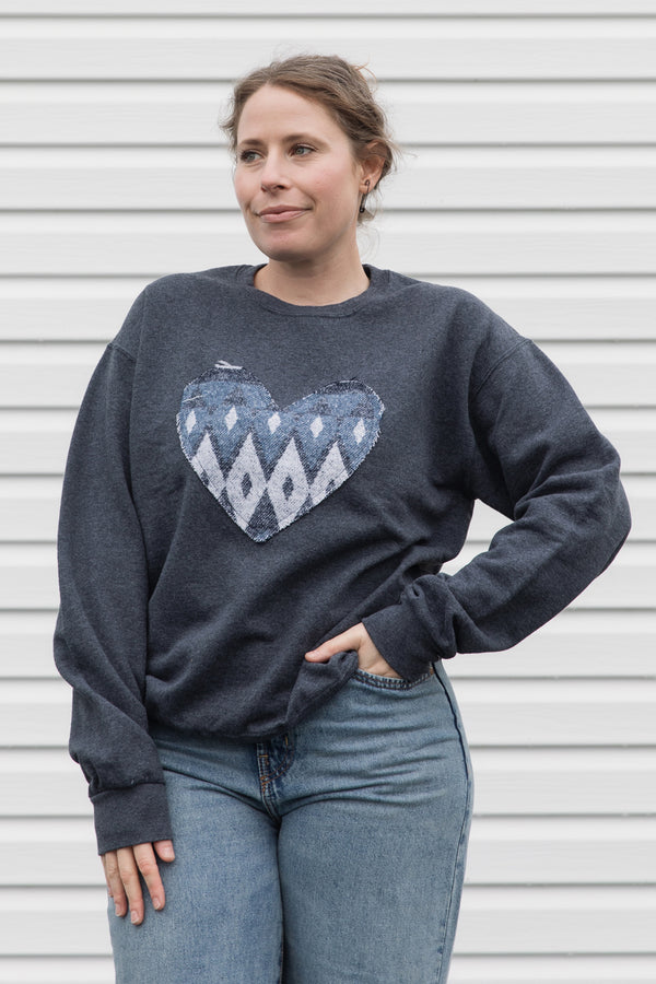 Woman wearing a charcoal grey sweatshirt with a blue heart design, sewn in canada