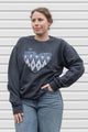 Woman wearing a charcoal grey sweatshirt with a blue heart design, sewn in canada