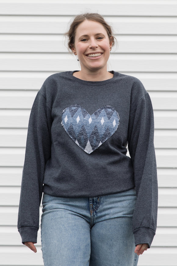 Woman wearing a charcoal grey sweatshirt with a blue heart design, sewn in canada