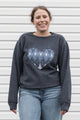 Woman wearing a charcoal grey sweatshirt with a blue heart design, sewn in canada
